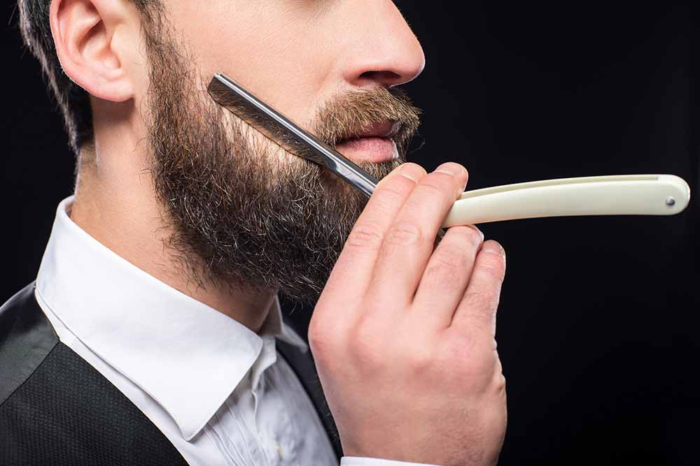 hombre perfilando la barba con una navaja de afeitar 