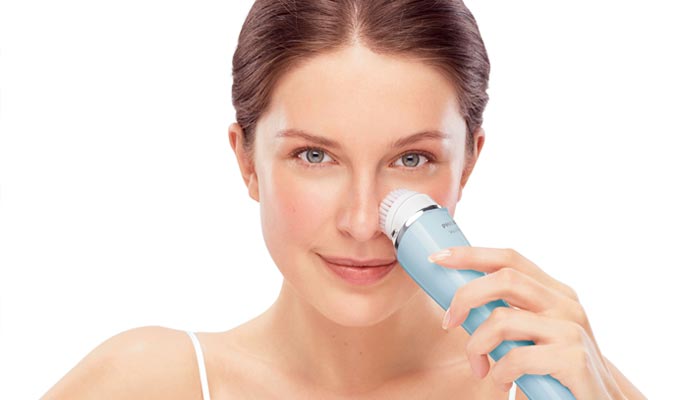 mujer utilizando un cepillo de limpieza facial eléctrico